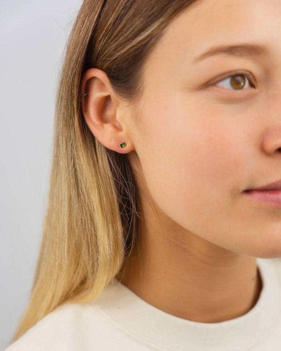 18ct gold stud earring with a small, rough green gemstone on a woman's ear.