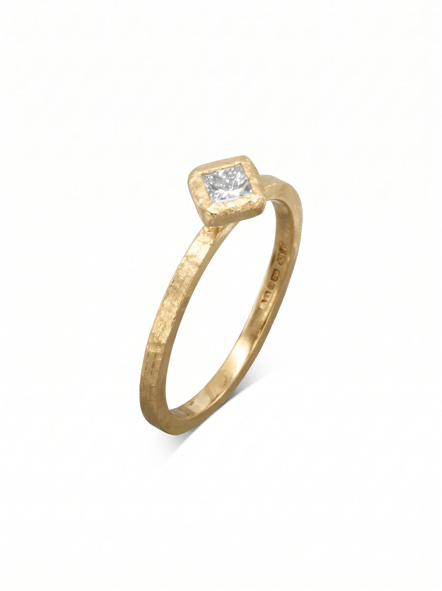 Gold engagement ring with a hammered texture and a square-cut diamond set in a bezel setting.