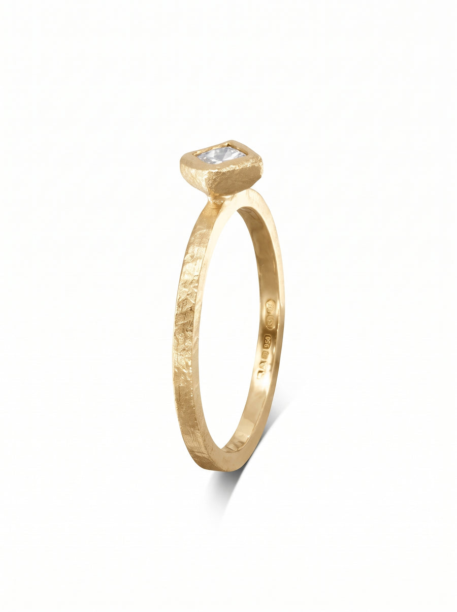 Dainty gold engagement ring with a hammered texture and a square-cut white gemstone in a bezel setting.