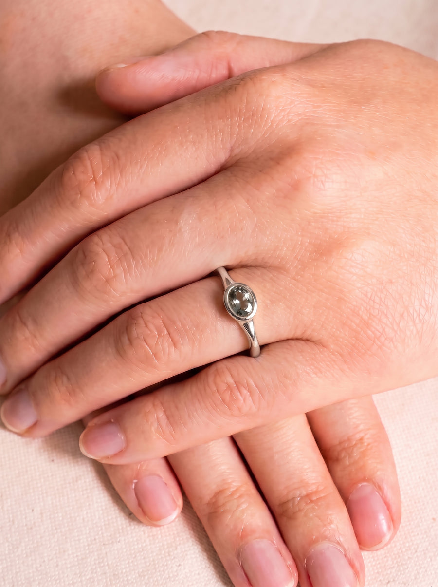 Oval sapphire engagement ring in a silver band worn on a finger.