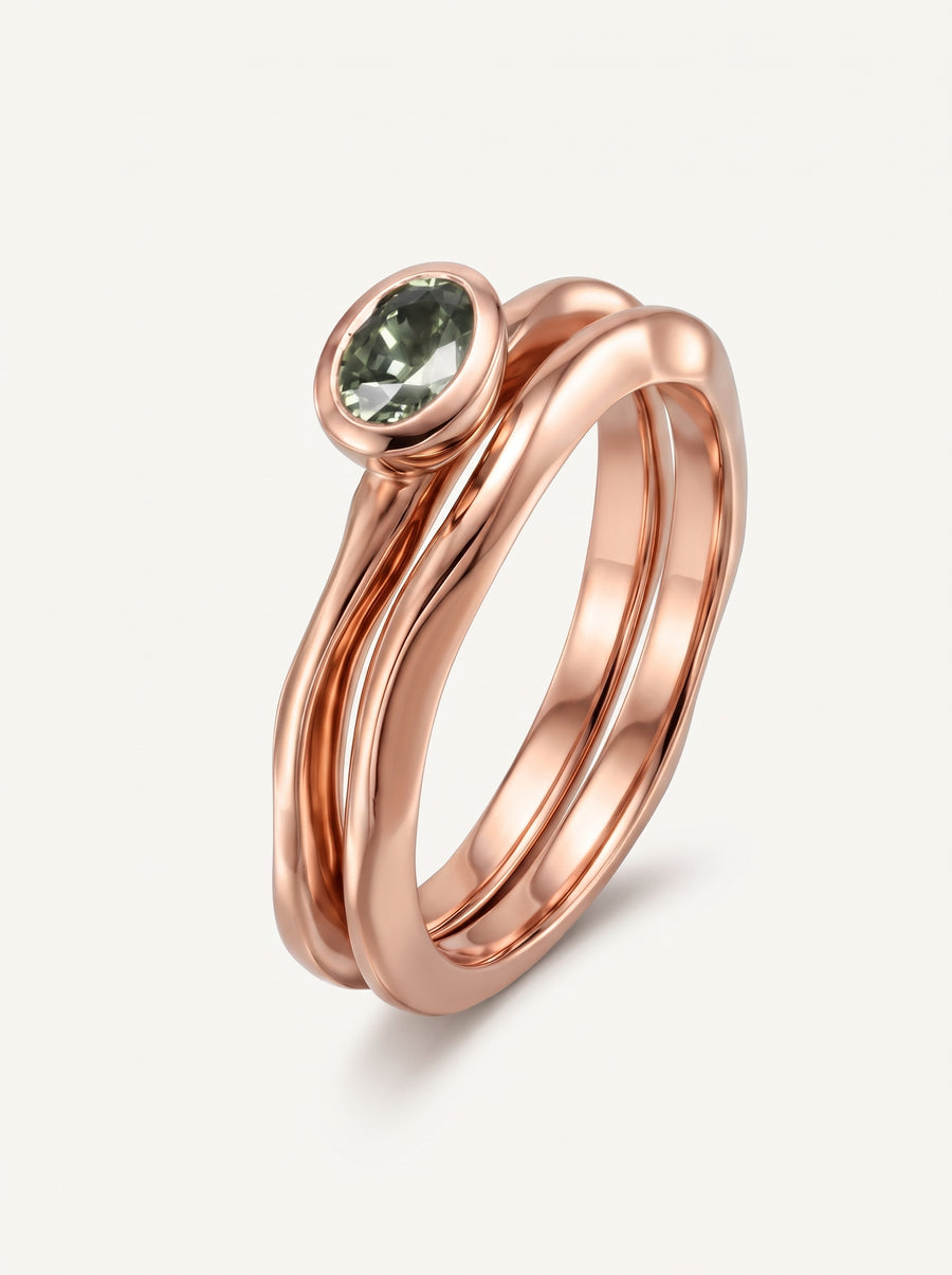 Rose gold engagement ring set featuring a bezel-set oval green sapphire on a wavy band.