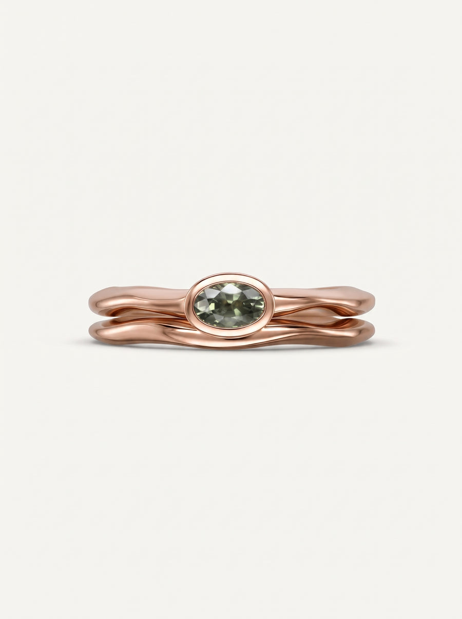 Rose gold engagement ring with an oval green sapphire in a bezel setting and a wavy band.