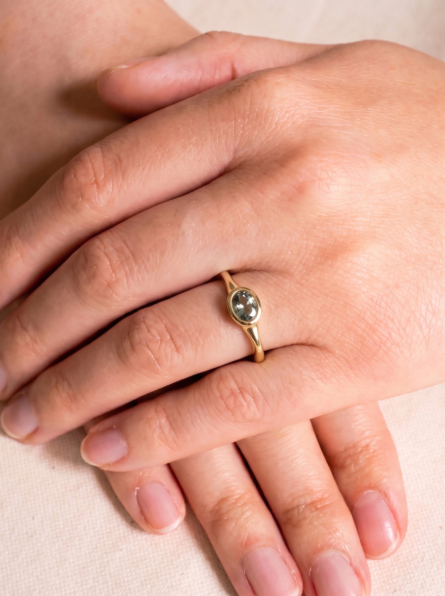 Gold ring featuring an oval-cut sapphire in a bezel setting worn on a finger.