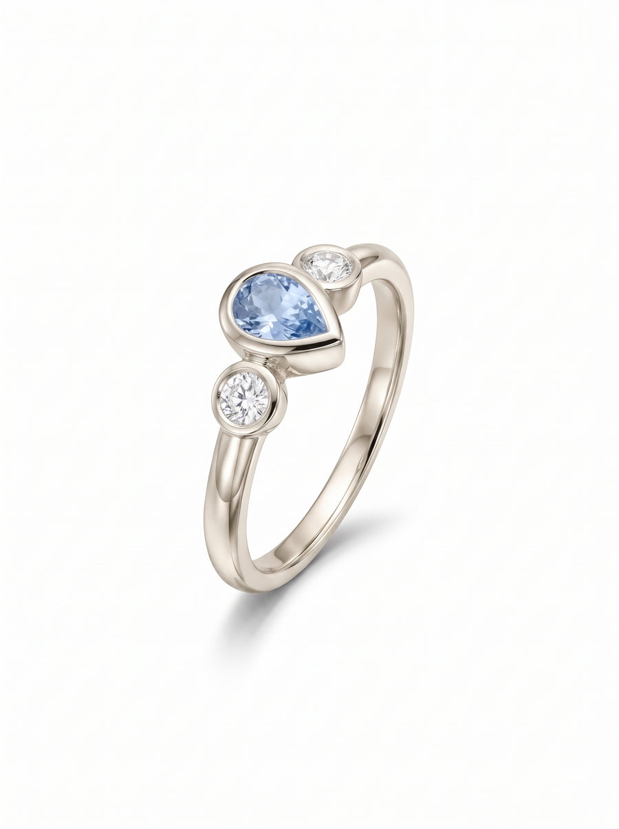 Trilogy ring in white gold featuring a pear-cut aquamarine flanked by two round diamonds in bezel settings.