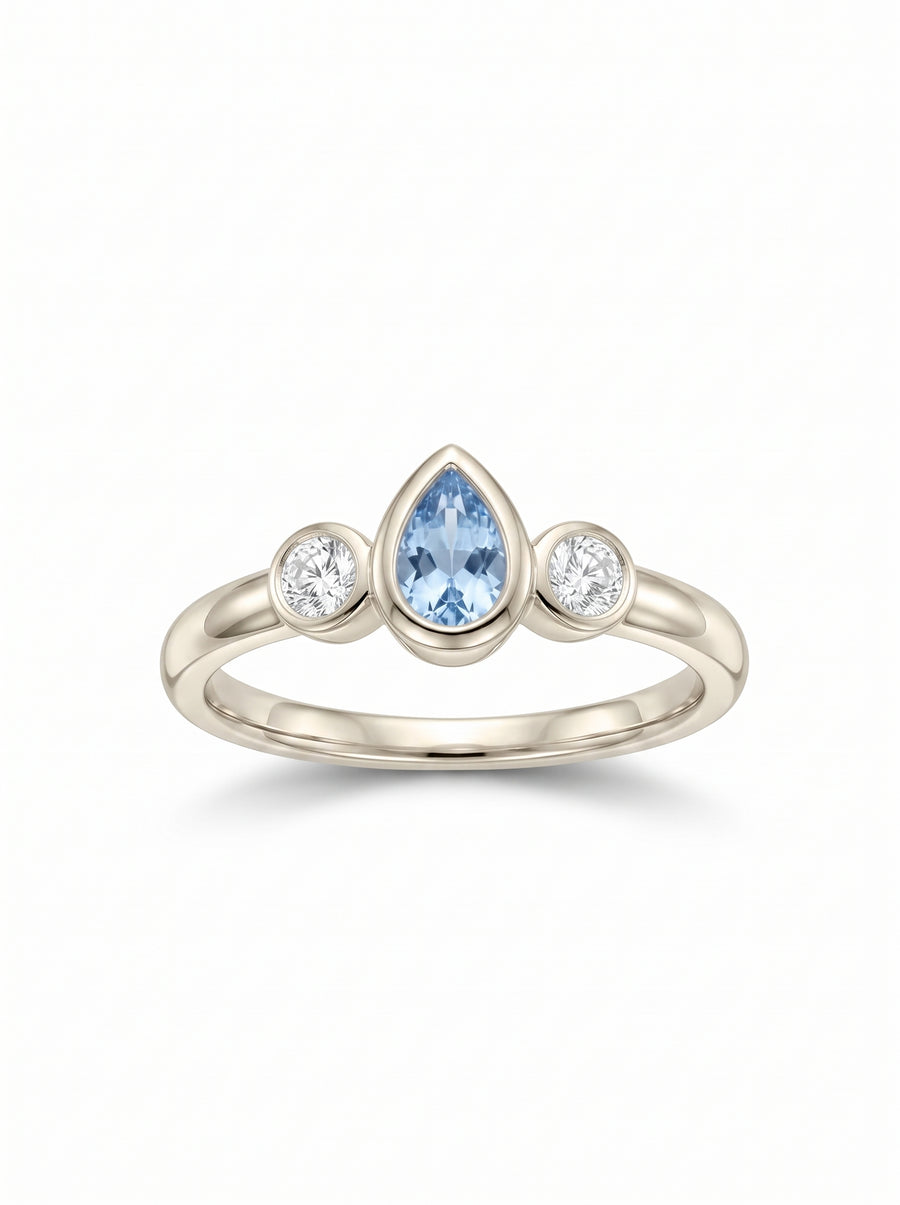 Trilogy ring in white gold featuring a pear-cut aquamarine flanked by two round diamonds in bezel settings.