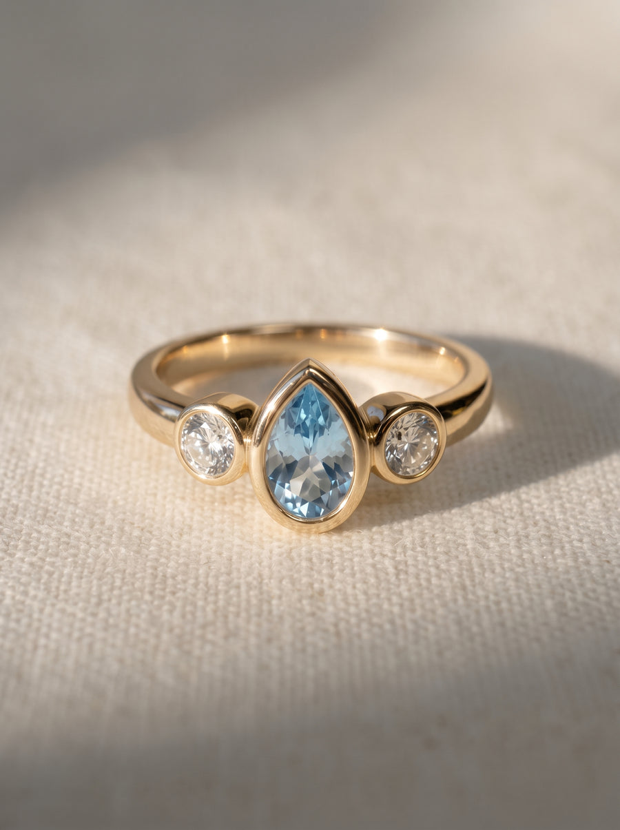 Trilogy engagement ring in 9ct yellow gold with a pear-cut aquamarine flanked by two round diamonds.