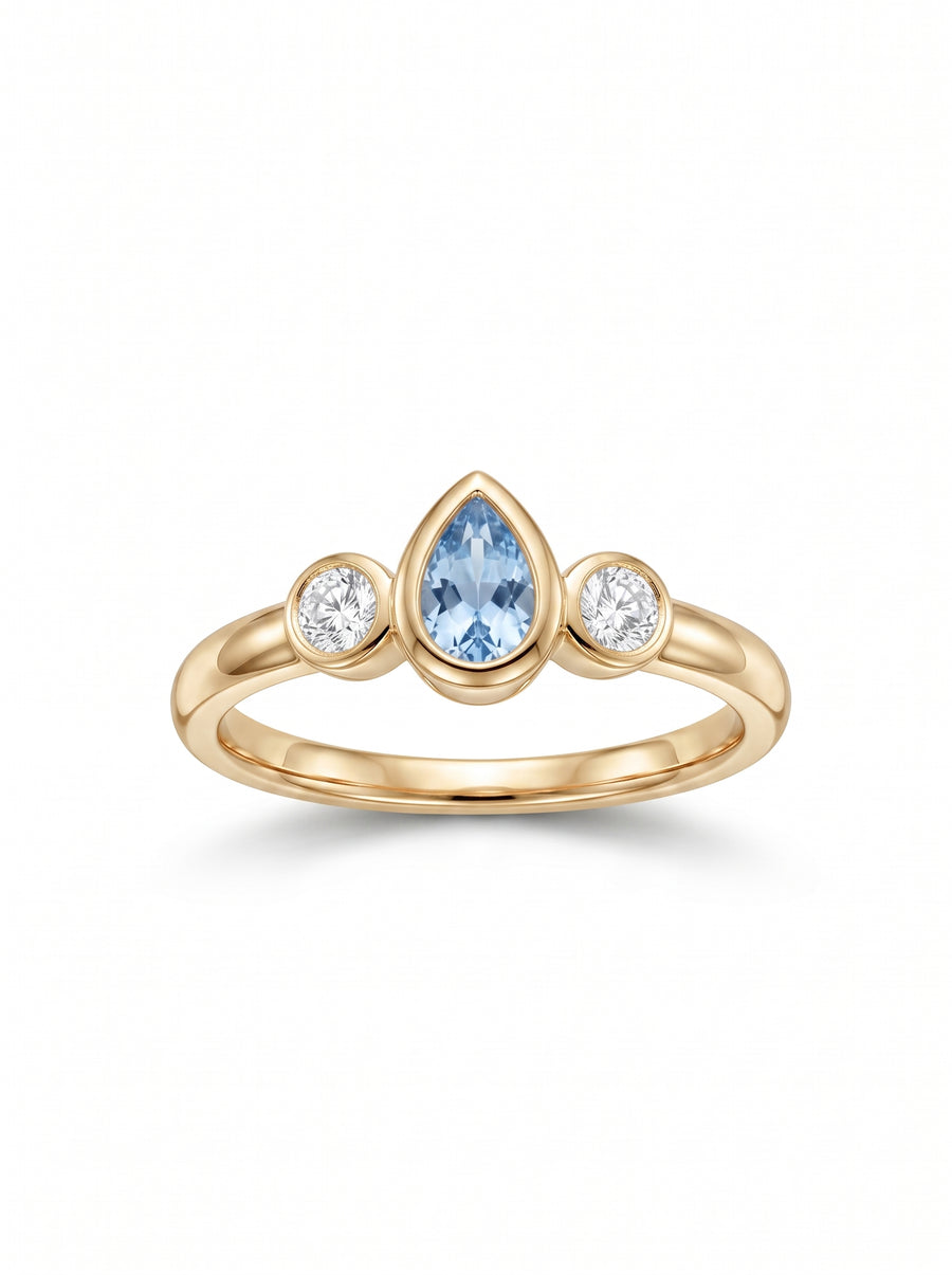 Gold trilogy ring featuring a pear-cut aquamarine flanked by two round diamonds in bezel settings.
