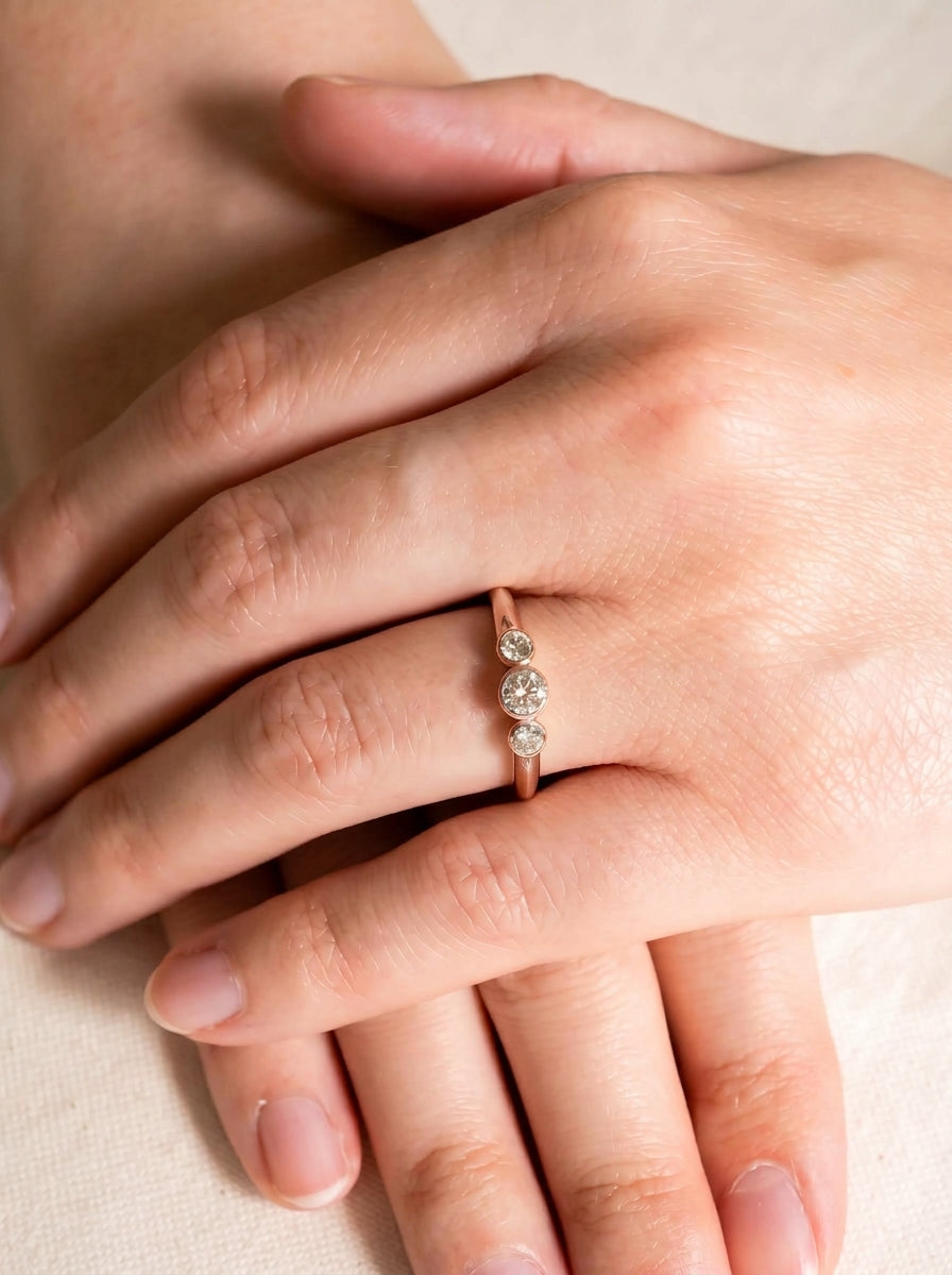 9ct gold trilogy engagement ring featuring three bezel-set round diamonds on a slender band worn on a finger.
