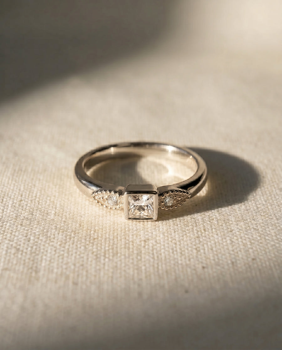 Platinum engagement ring with a square diamond and two small side diamonds.