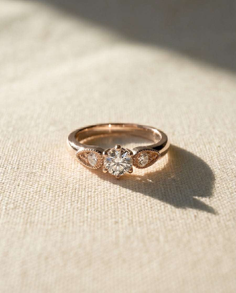 18ct rose gold engagement ring with a round diamond and two smaller side diamonds.