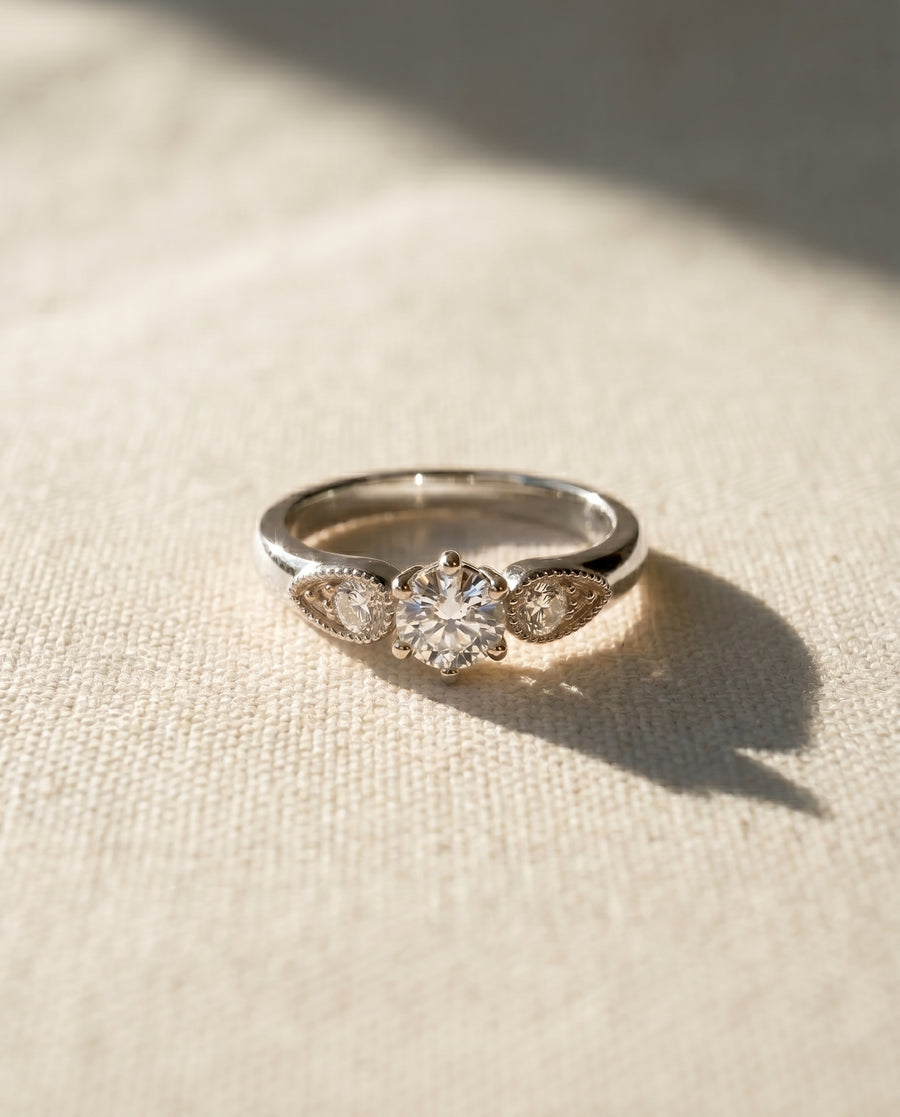 Platinum vintage shoulder engagement ring with a round diamond and two pear-shaped side stones.