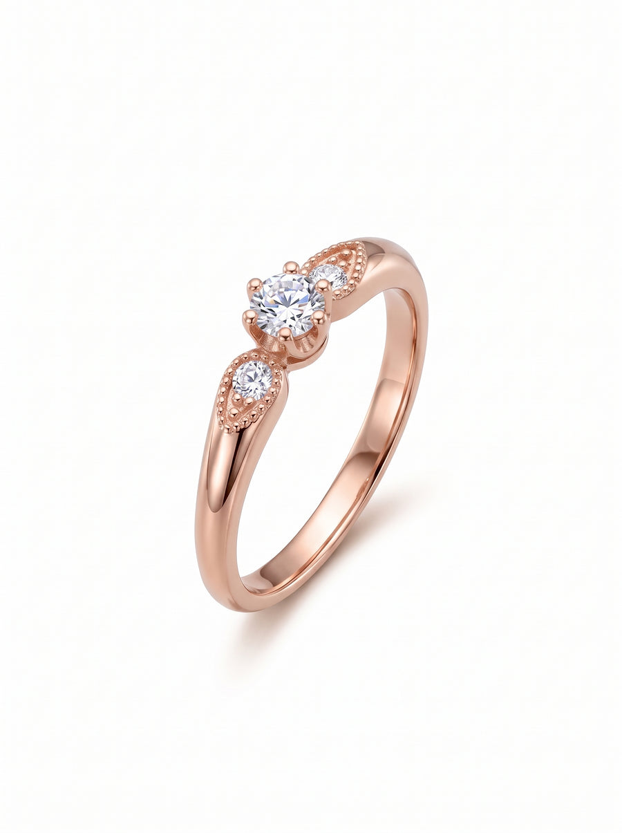 Rose gold engagement ring with three round diamonds and vintage-style milgrain detailing on the shoulders.