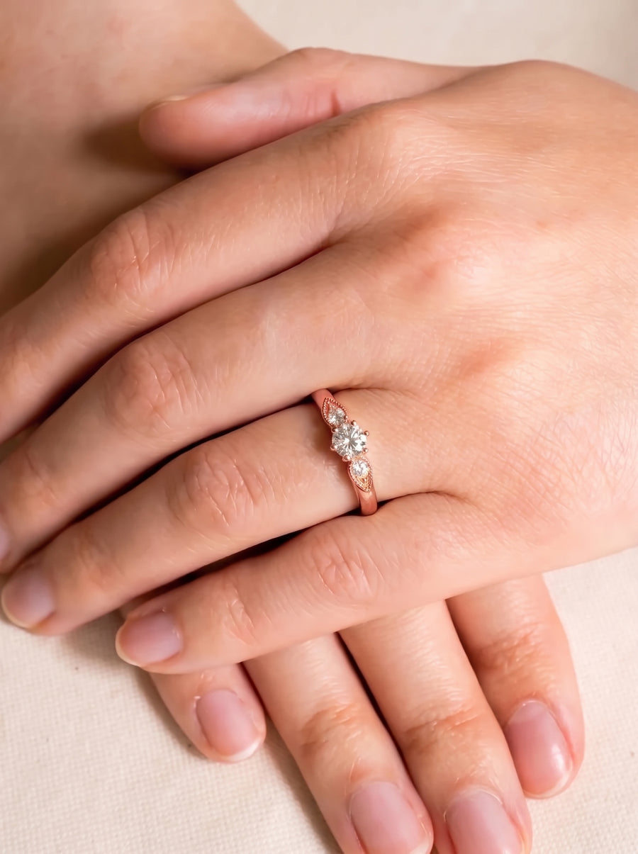 Rose gold engagement ring with three round diamonds and vintage-style leaf detailing on the band.