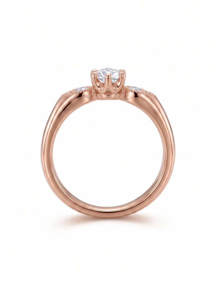 Rose gold engagement ring with a round center diamond and small accent stones on the vintage-style shoulders.