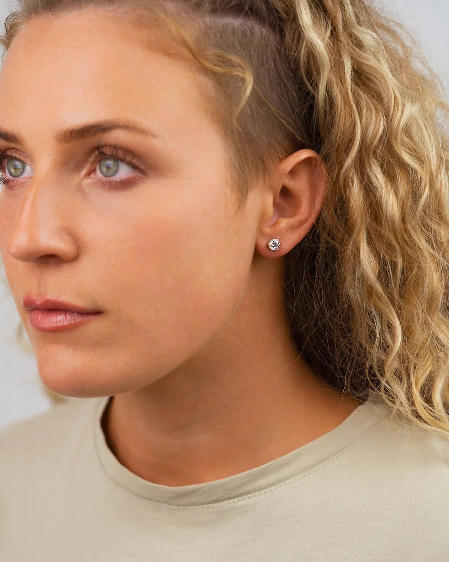 Woman wearing a three-claw gold stud earring with a round diamond, natural look