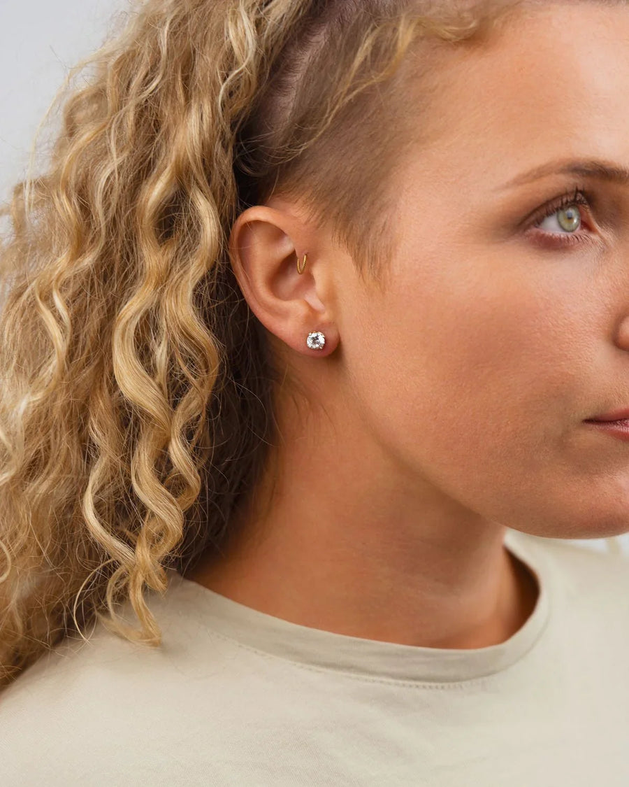 Woman wearing three-claw diamond gold stud earrings with a gold hoop, luxury handmade jewellery