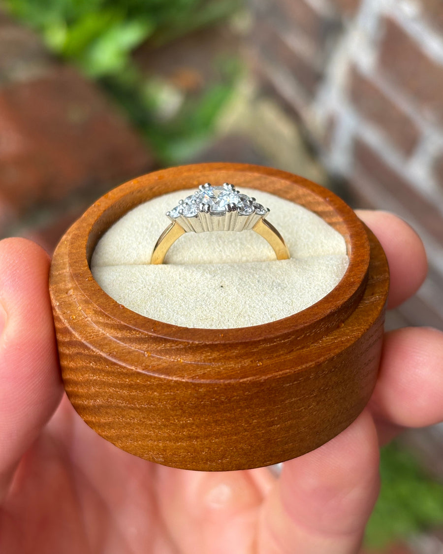 Round cut diamond engagement ring with a trefoil claw setting on a yellow gold band in a wooden box.