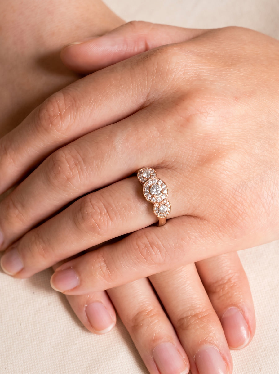 Rose gold trilogy engagement ring featuring three round diamond cluster settings on a woman's finger.