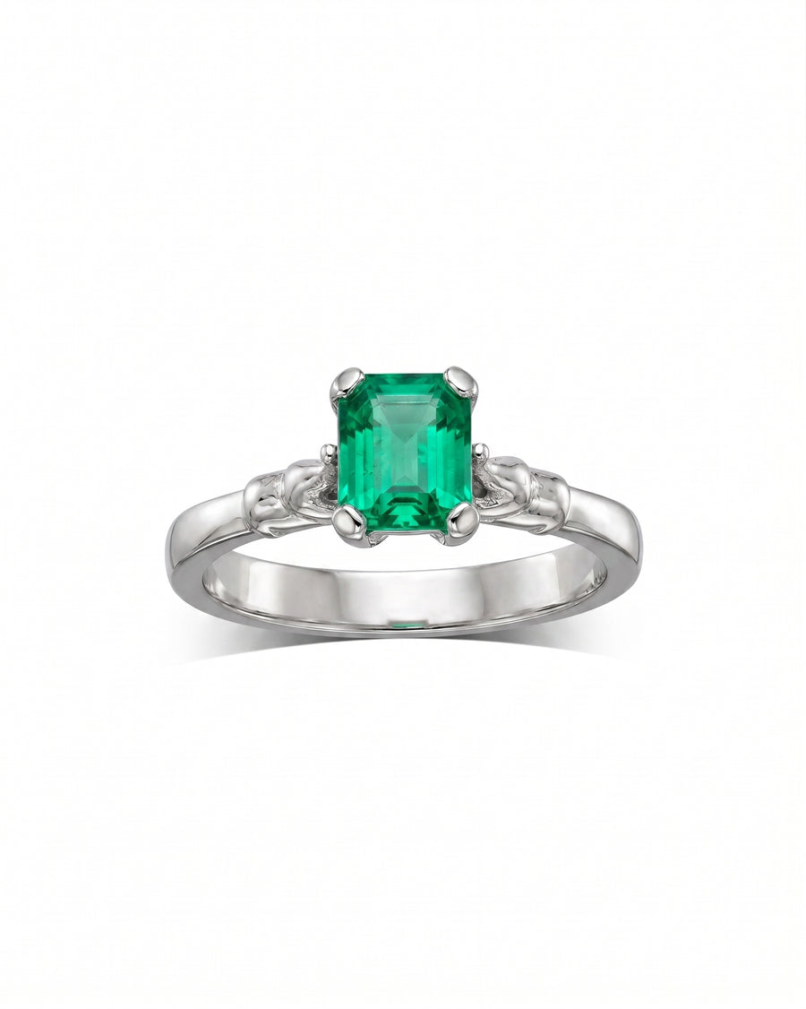 White gold engagement ring with a square emerald and elephant motif shoulders.