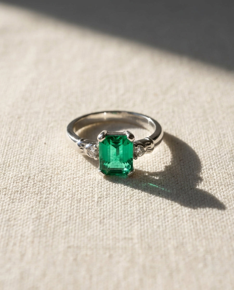 Platinum ring with an emerald-cut emerald and two small side diamonds.