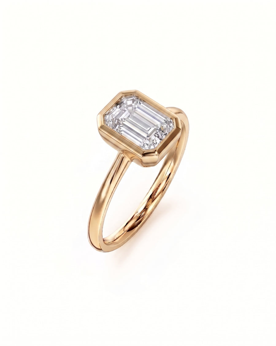 Gold engagement ring with an emerald cut diamond in a bezel setting.