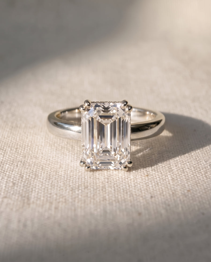 Emerald-cut diamond solitaire engagement ring set in a polished silver-toned metal cathedral band.