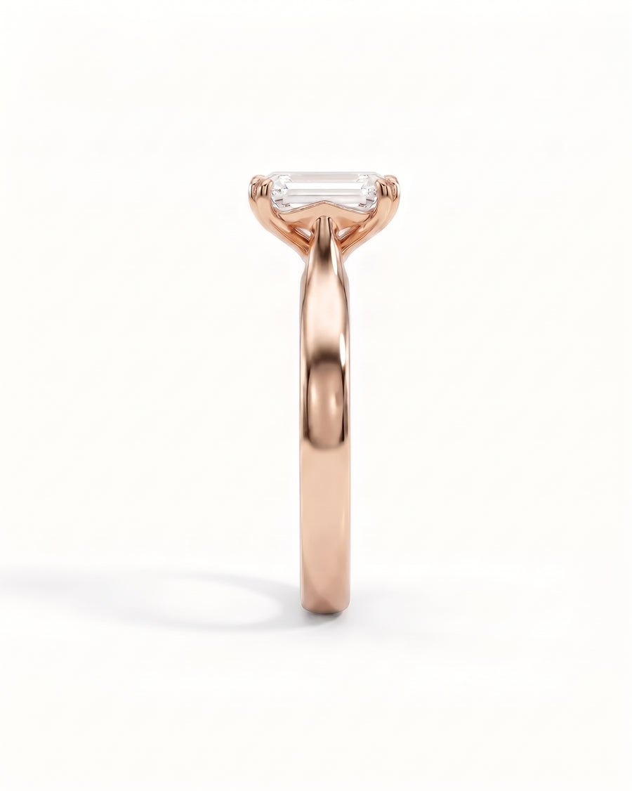 Emerald-cut diamond solitaire engagement ring set in a rose gold cathedral band.