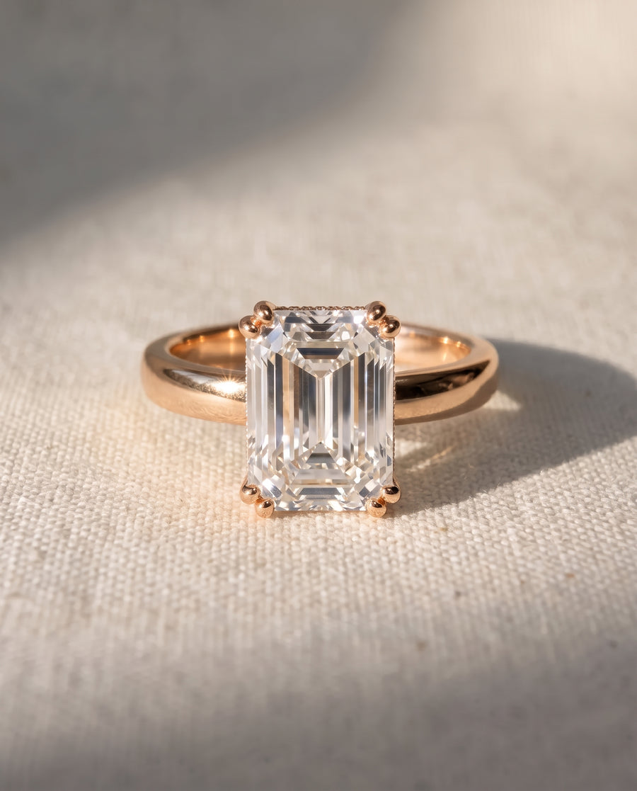 Emerald-cut diamond solitaire engagement ring set in a polished rose gold cathedral band.