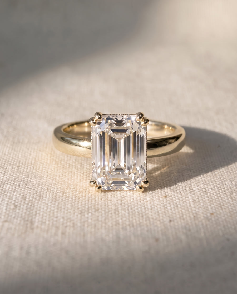Emerald-cut diamond solitaire engagement ring set in a polished yellow gold cathedral band.