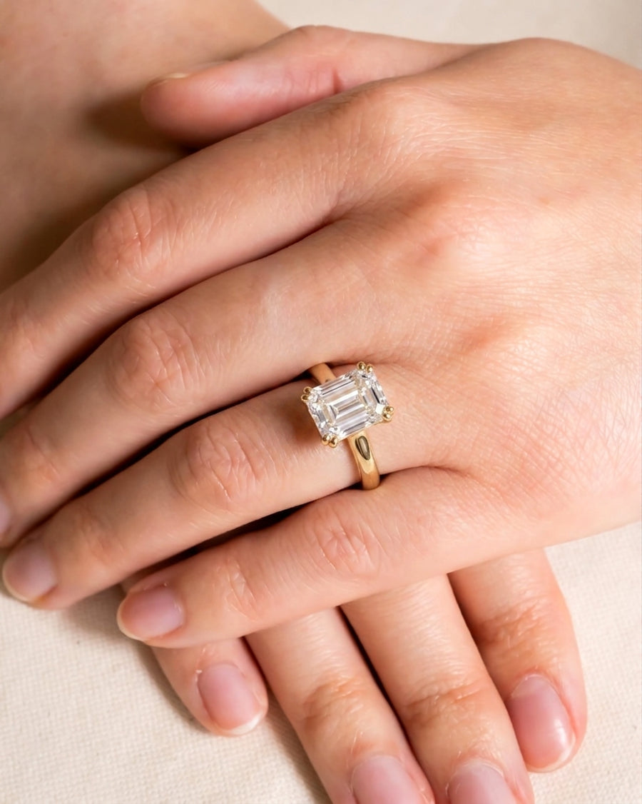 Gold cathedral solitaire engagement ring with an emerald-cut diamond on a hand.