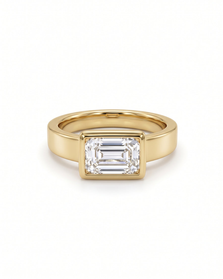 Emerald cut diamond engagement ring in a yellow gold bezel setting on a white background.