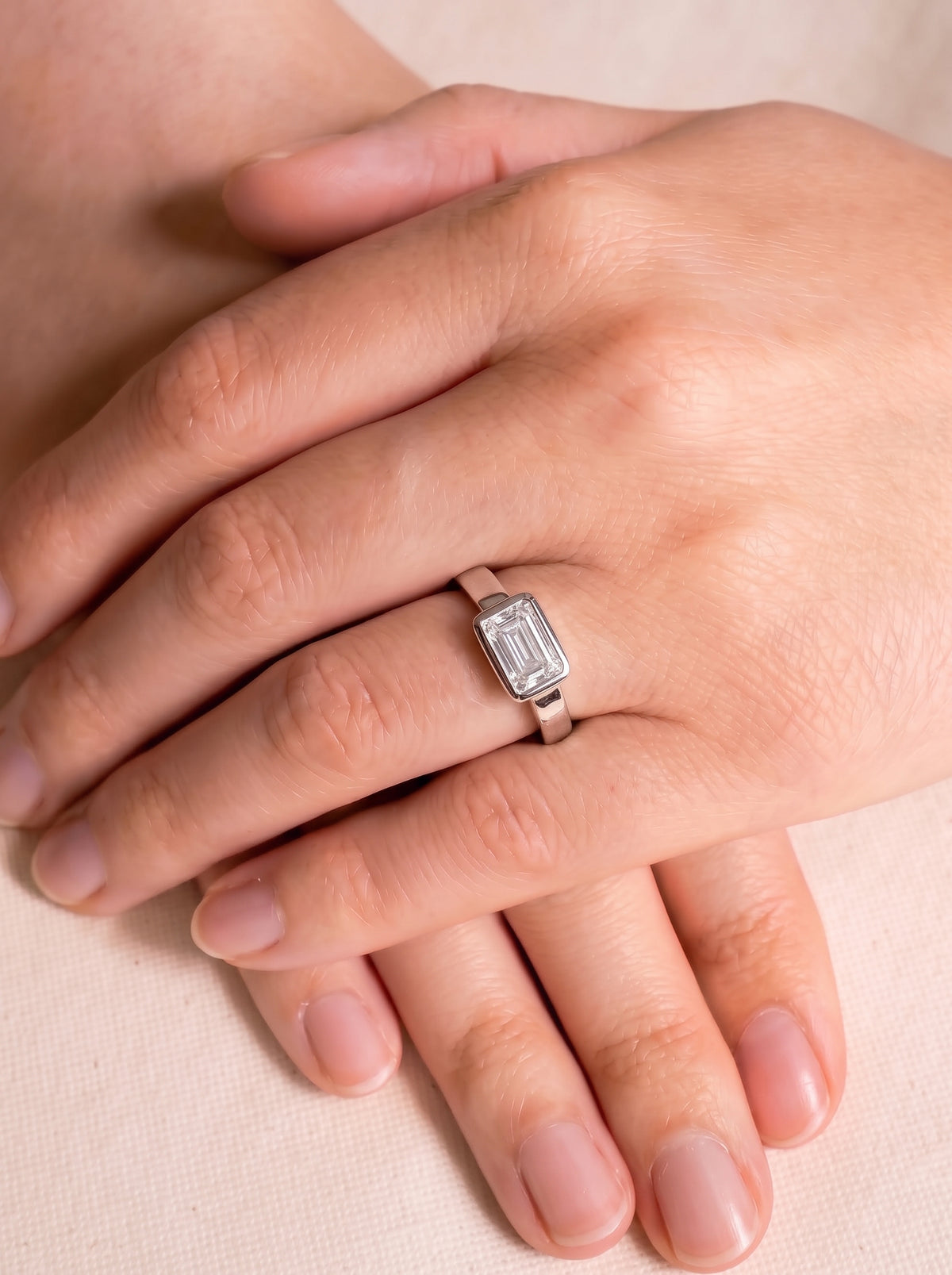 Emerald cut diamond engagement ring in a platinum bezel setting worn on a finger.