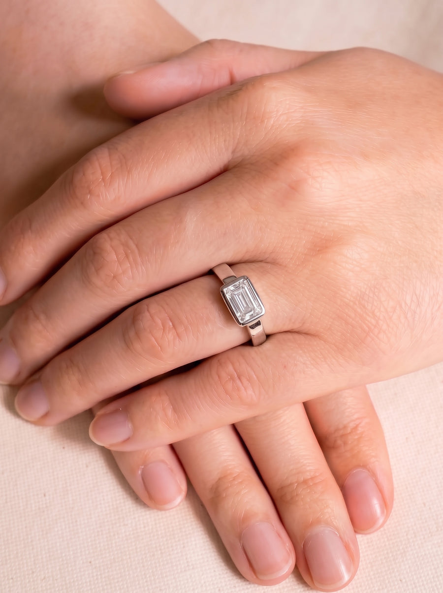 Emerald cut diamond engagement ring in a platinum bezel setting worn on a finger.