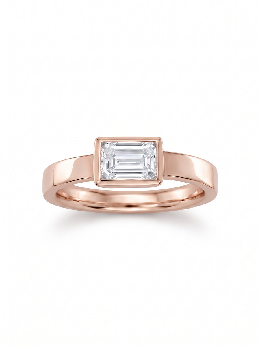 Emerald cut diamond engagement ring in a rose gold bezel setting on a plain band.