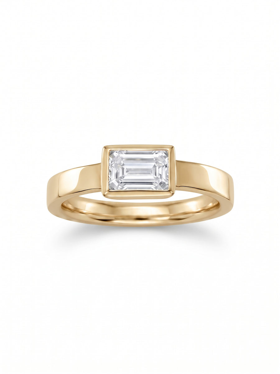 Emerald cut diamond engagement ring in a yellow gold bezel setting on a white background.