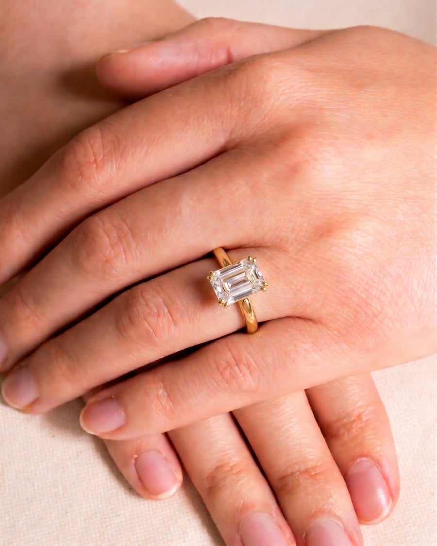 Gold engagement ring with an emerald cut diamond and hidden halo.