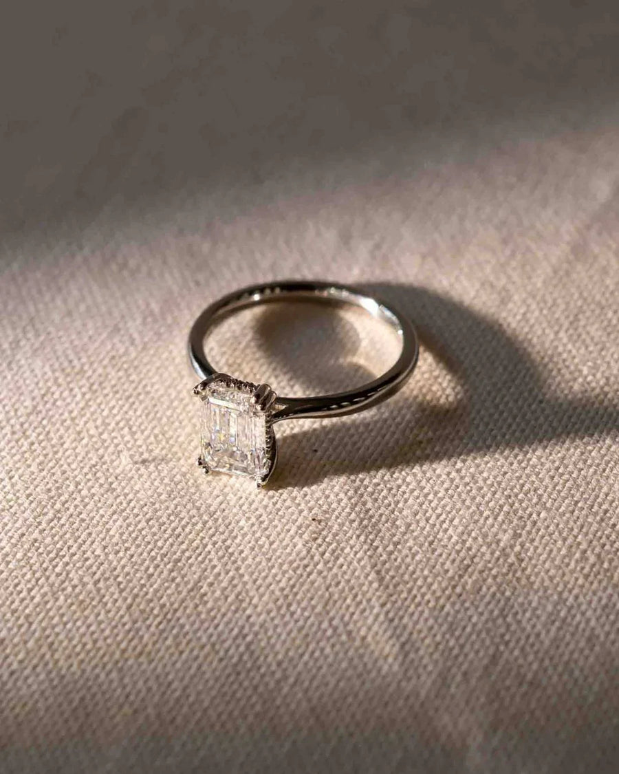 Silver engagement ring with an emerald cut diamond and hidden halo.