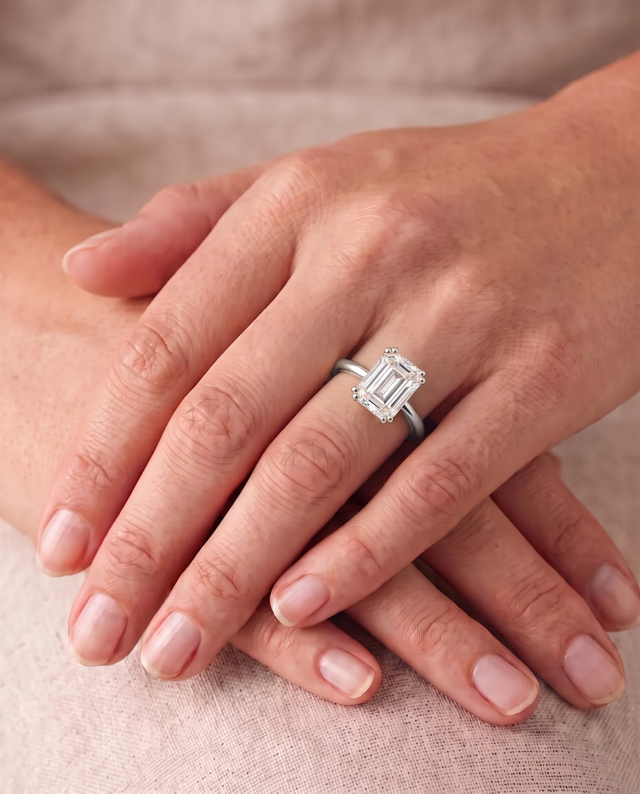 Emerald cut diamond engagement ring with a hidden halo on a polished silver band worn on a finger.