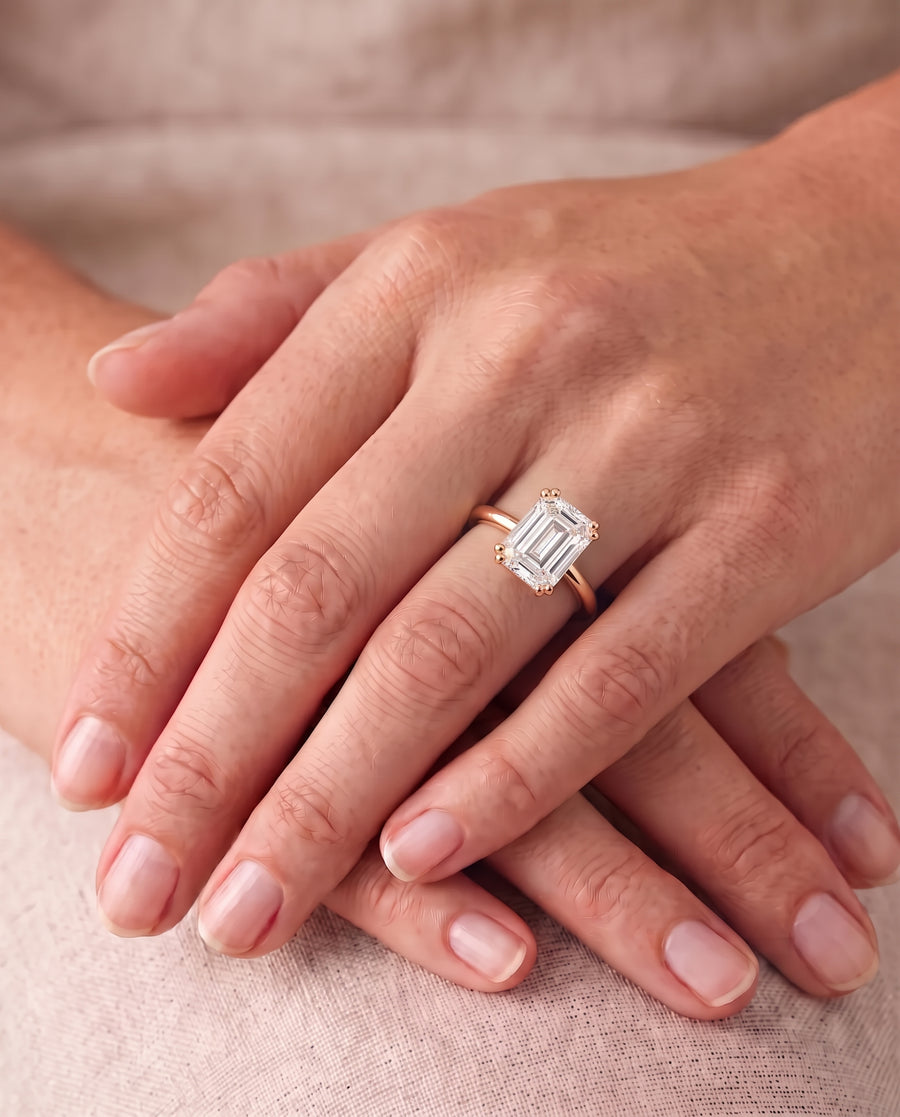 Emerald cut diamond engagement ring with a hidden halo on a rose gold band worn on a finger.