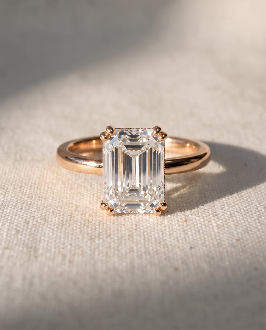 Emerald cut diamond engagement ring with a hidden halo set in a polished rose gold band.