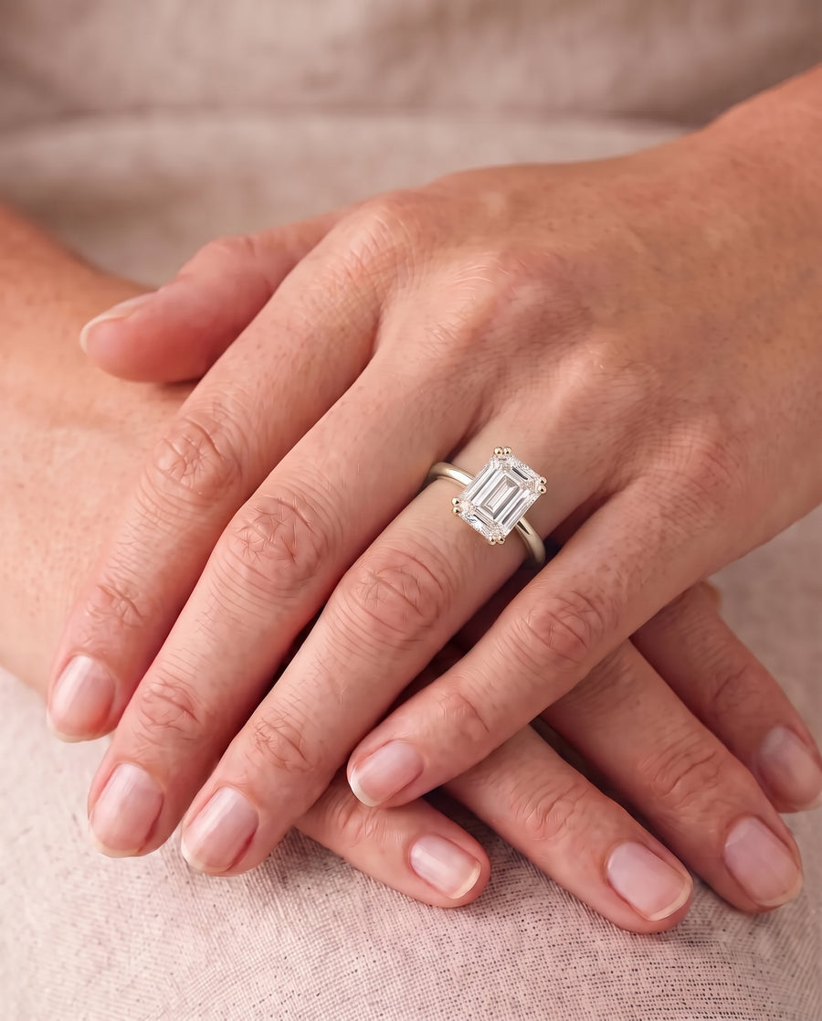 Emerald cut diamond engagement ring with a hidden halo on a gold band worn on a finger.