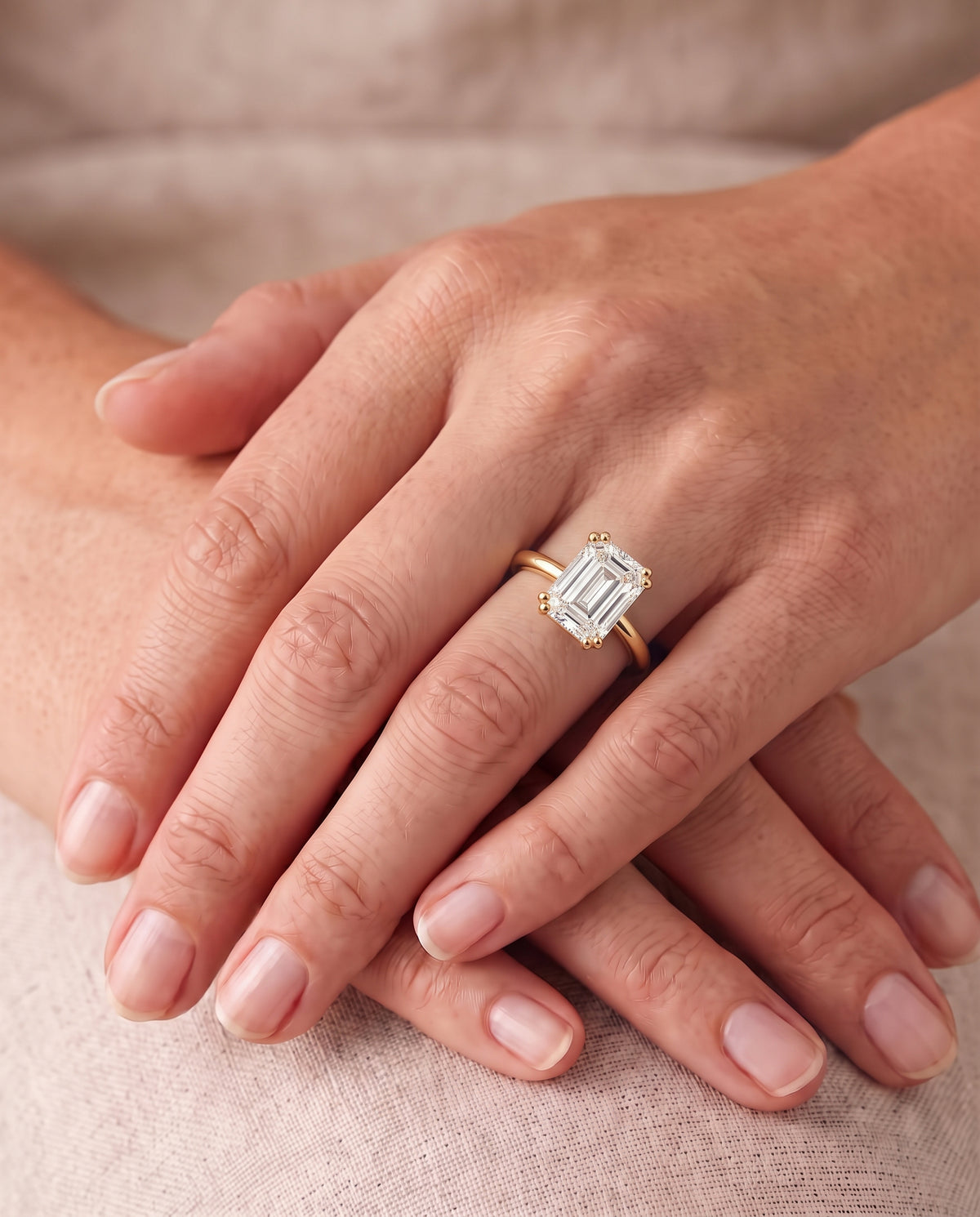 Emerald cut diamond engagement ring with a hidden halo on a yellow gold band worn on a finger.
