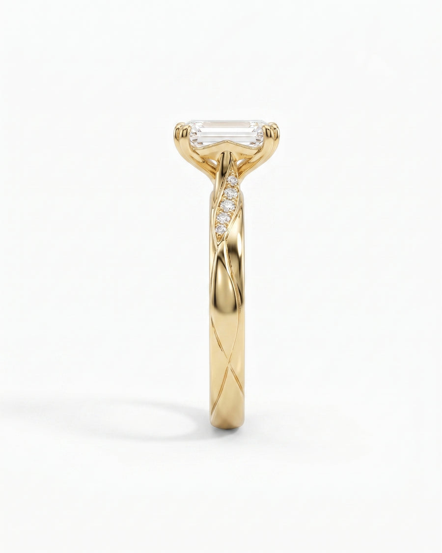 Gold engagement ring with an emerald cut diamond and pavé accents on a twisted band.