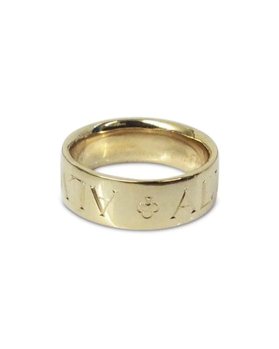 Gold wedding ring with engraved letters on a plain white background