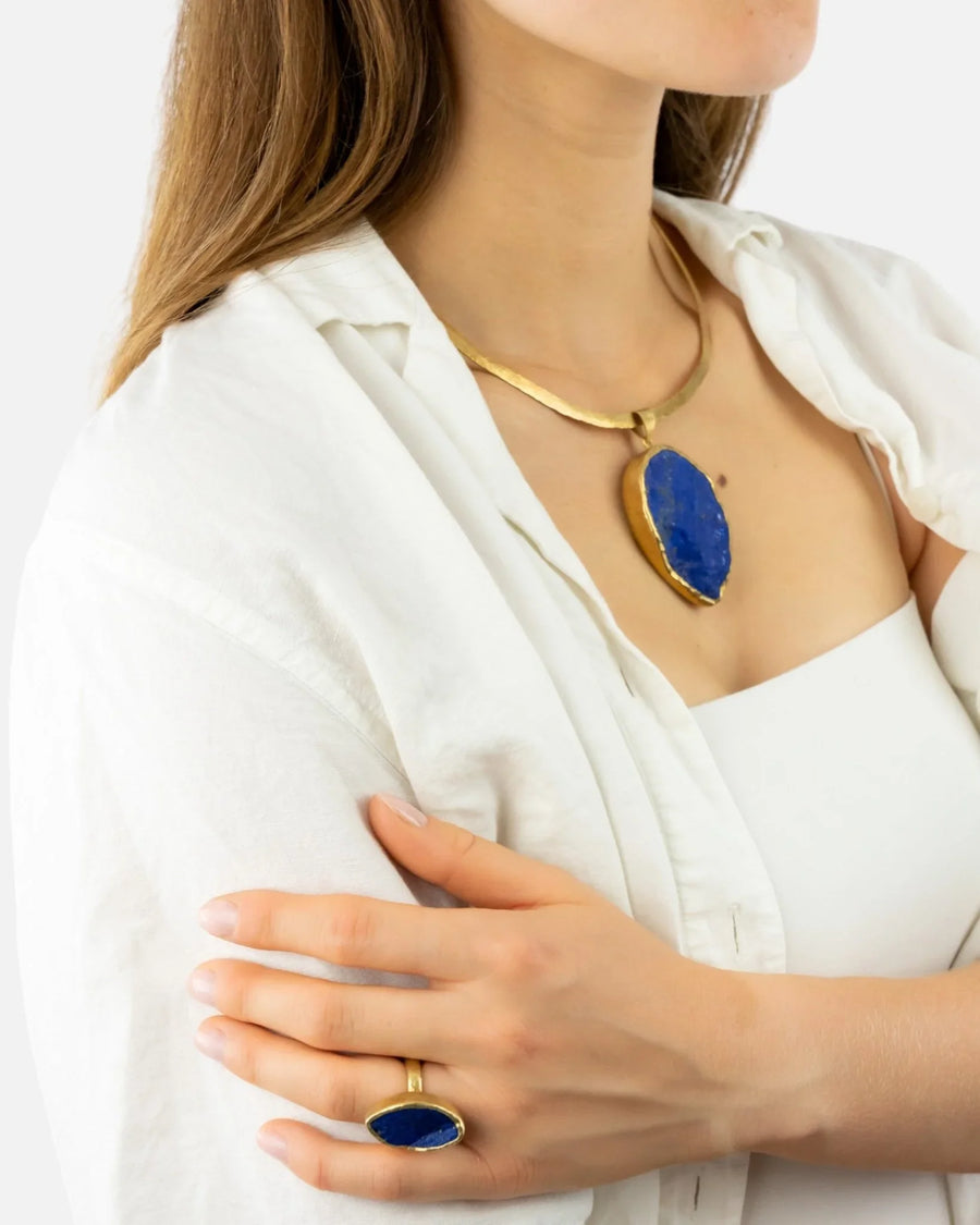 Woman wearing a handmade gold necktorc with a blue lapis lazuli pendant and matching ring