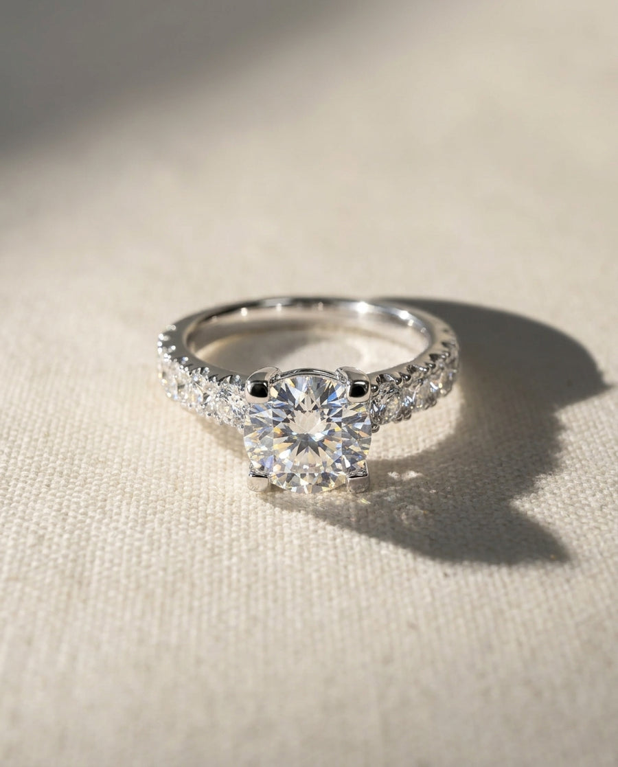 Silver fishtail set engagement ring with a round center diamond and pavé band.