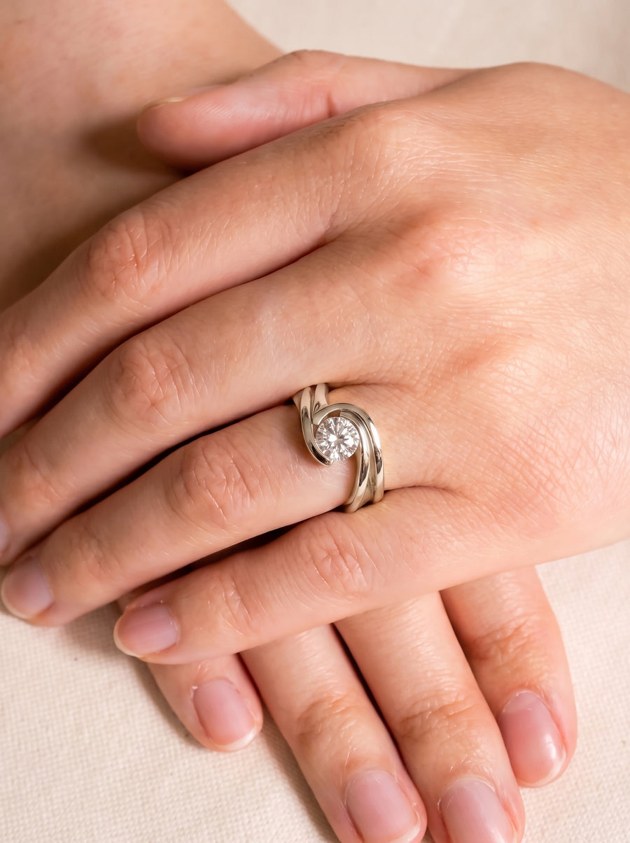 Round diamond engagement ring with a flat twist band in polished white gold worn on a finger.