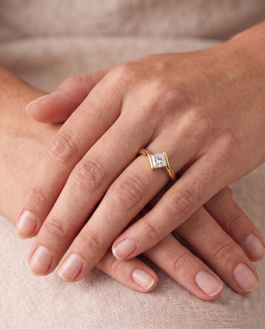 Princess cut diamond engagement ring with a flat twist gold band worn on a finger.