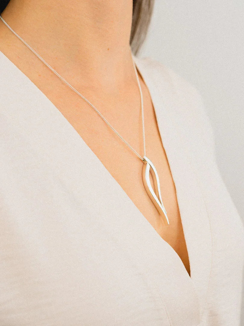 Handmade silver pendant necklace with organic shape on woman in cream v-neck top