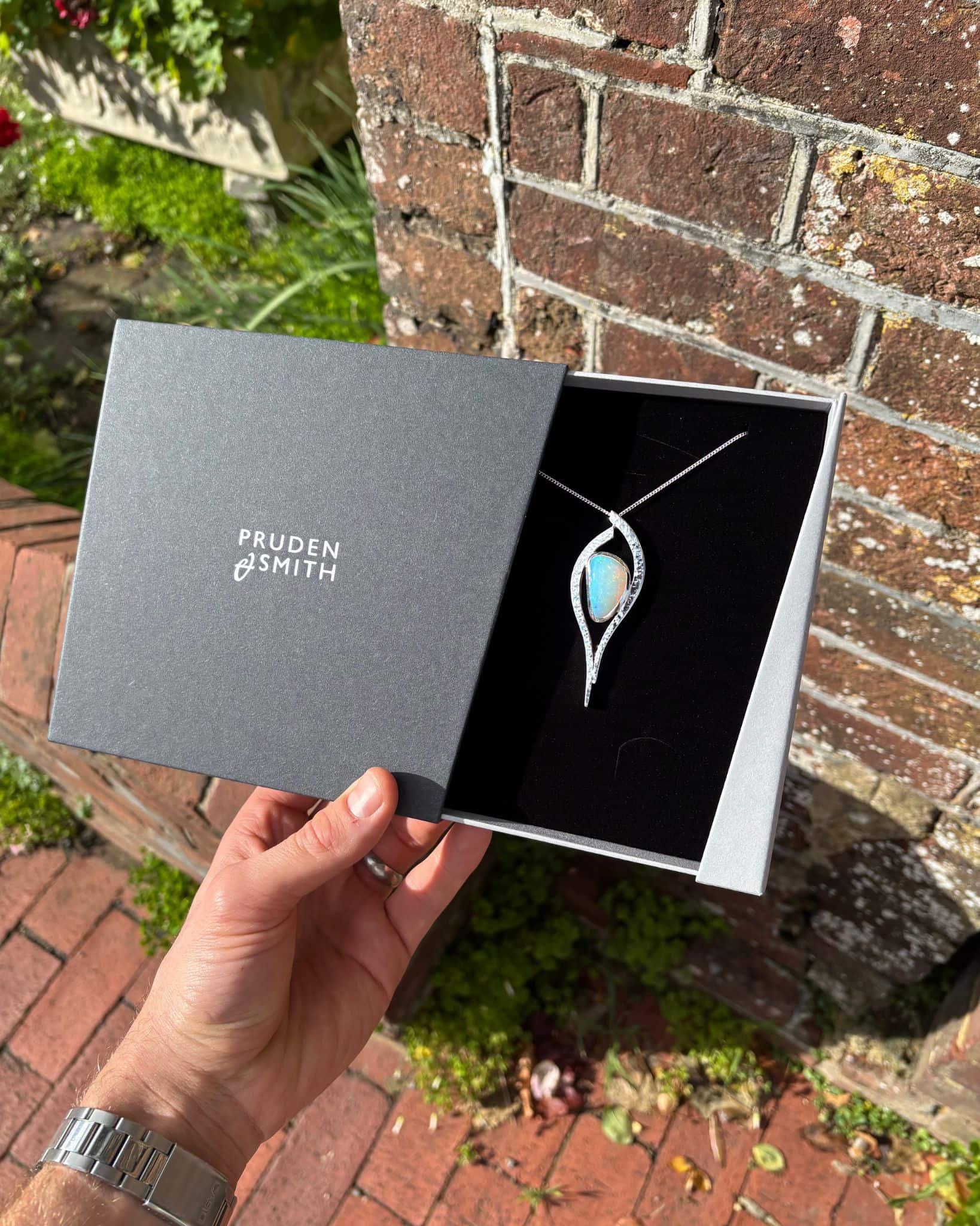 Hand holding a luxury jewellery box with a unique pendant necklace outdoors